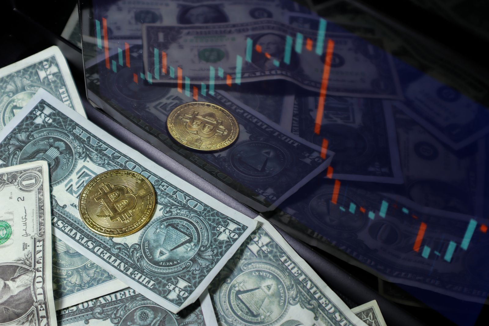 Moeda de Bitcoin apoiada sobre notas de dólar com gráfico de mercado ao fundo