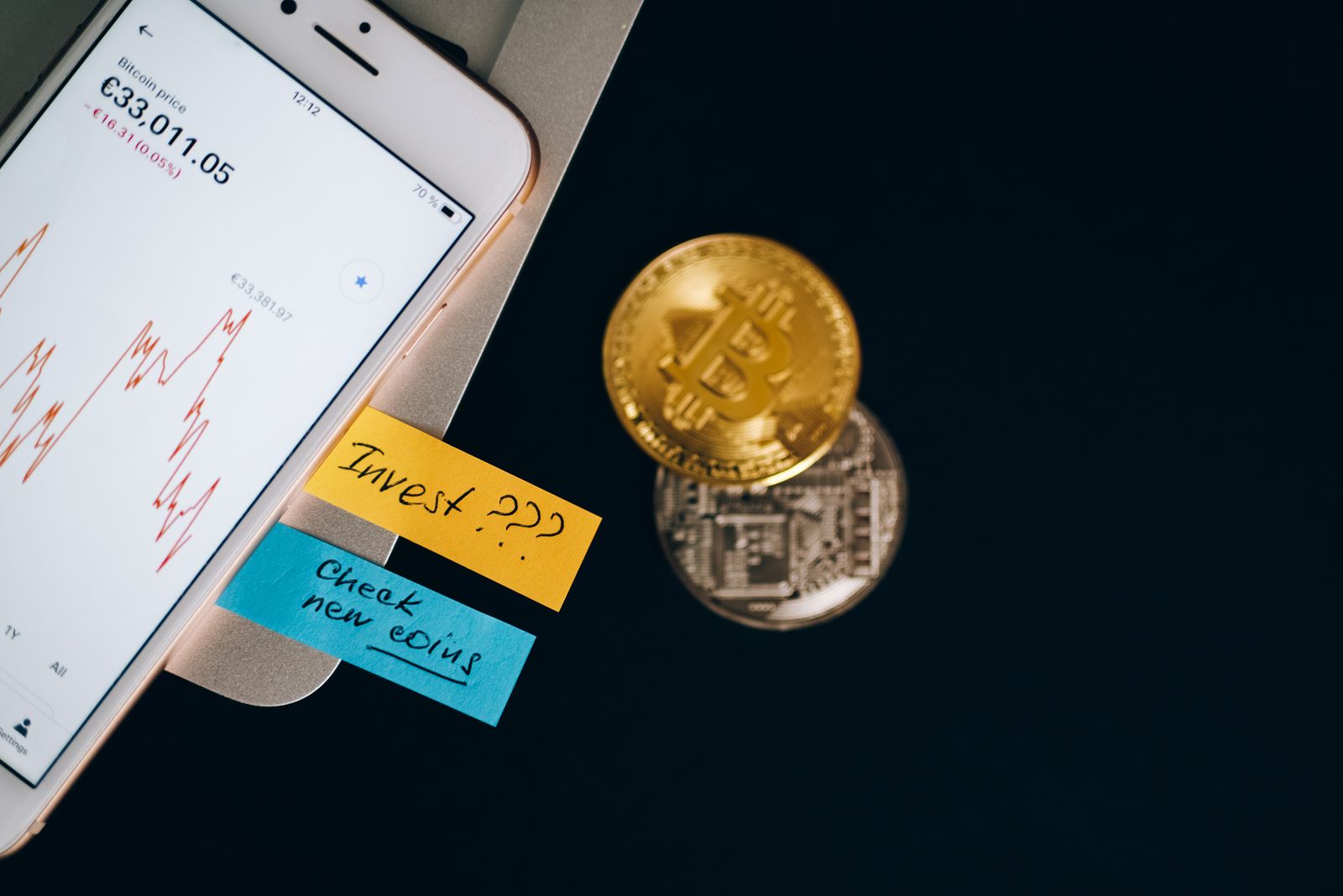 Moedas de bitcoin sobre um smartphone exibindo gráfico de preço, simbolizando a correção do BTC para US$ 77 mil e a compra agressiva das baleias