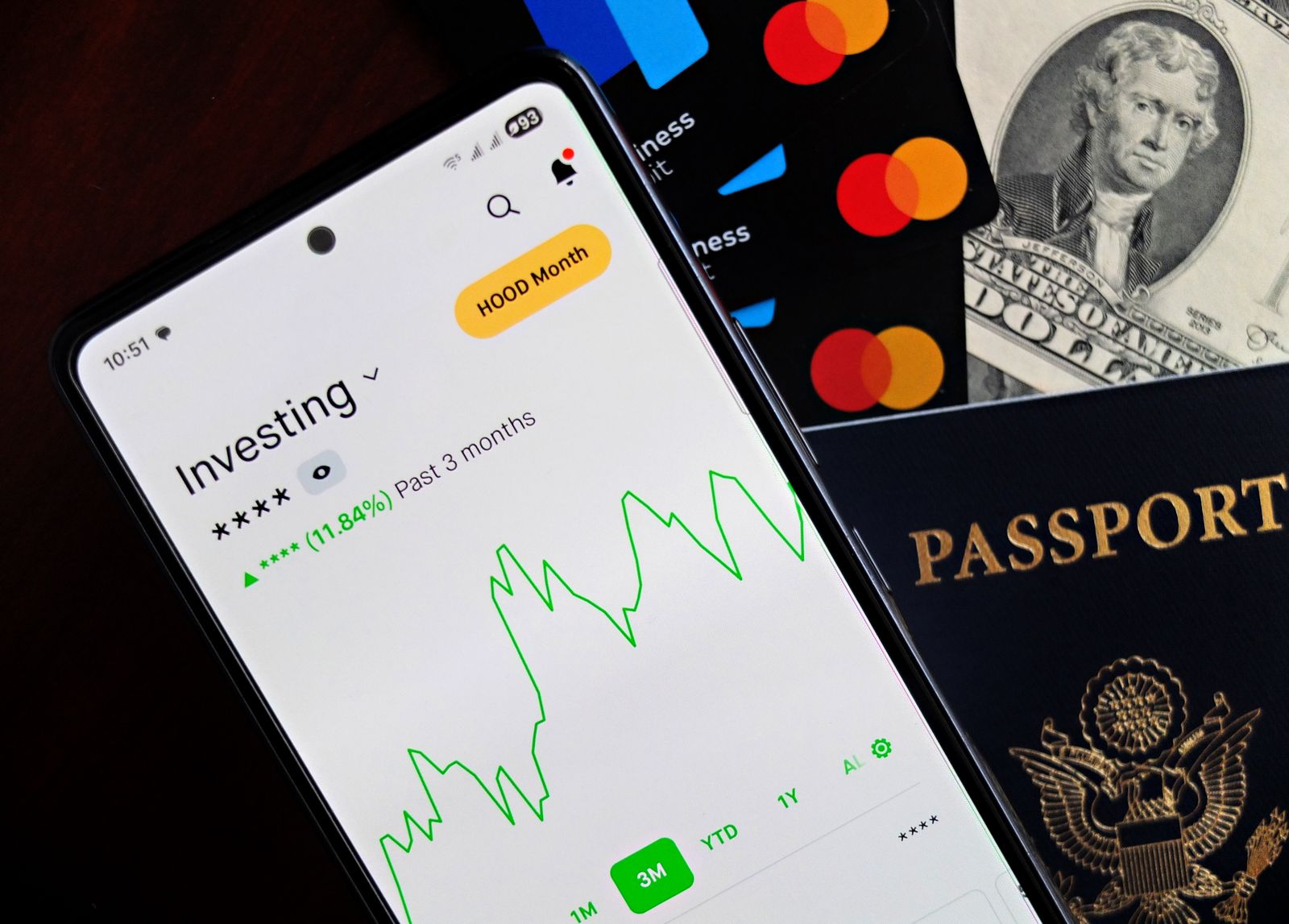 Smartphone exibindo um aplicativo de investimentos sobre cartões e cédulas.